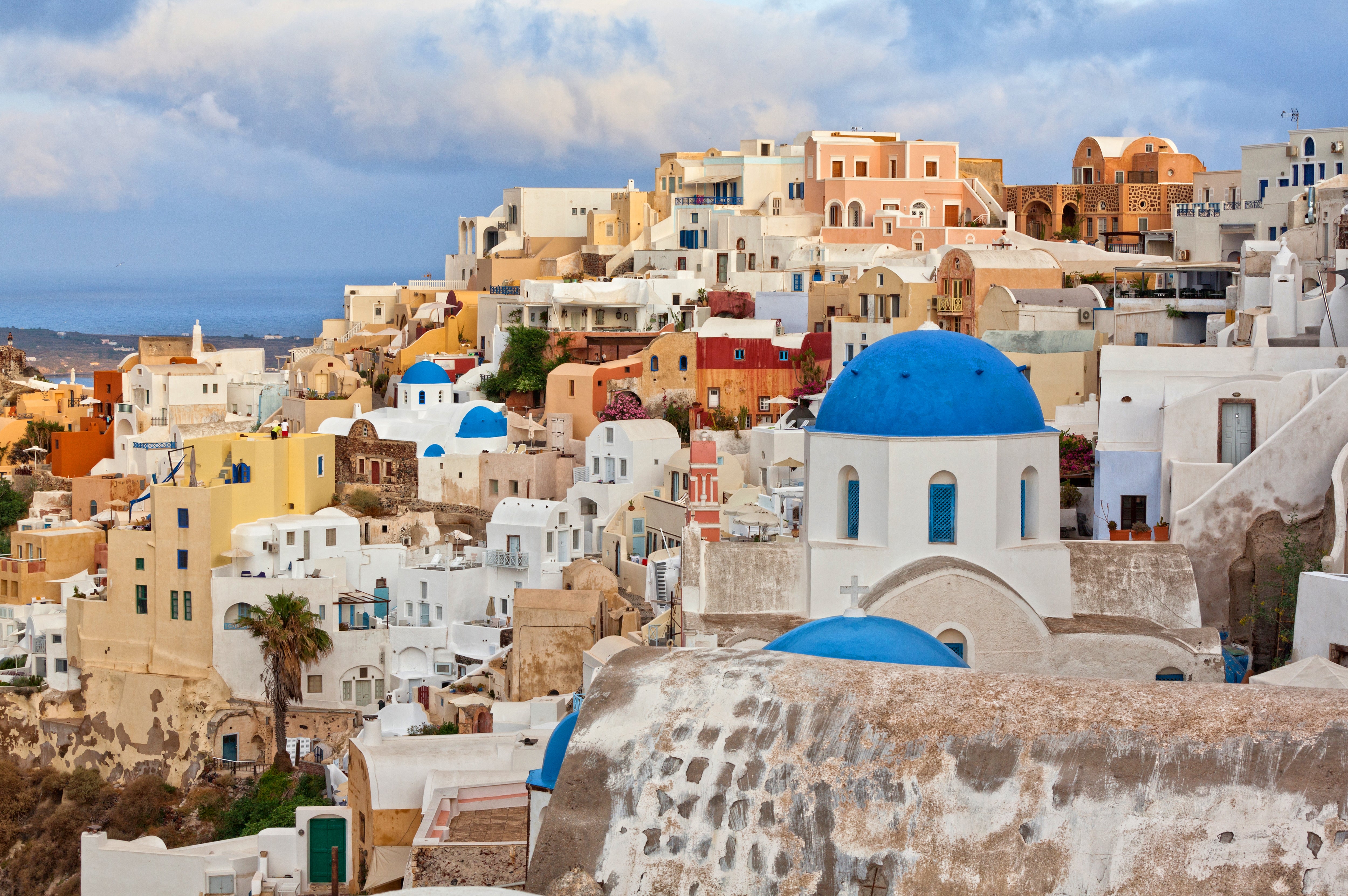 Typische weiß getünchte Häuser mit blauen Kuppeln und Meerblick in einer Küstenstadt unter wolkigem Himmel.