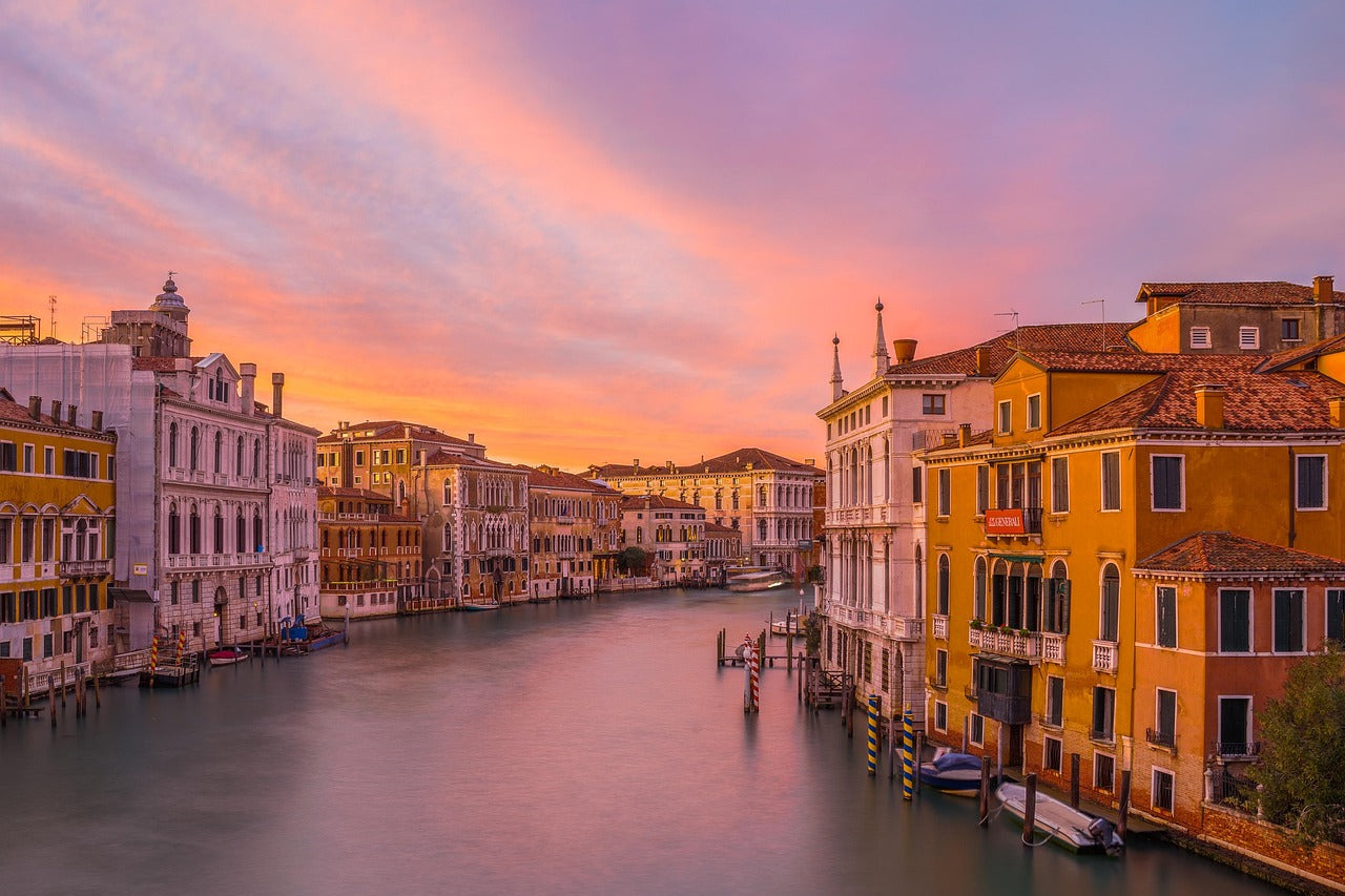 Blick auf einen venezianischen Kanal mit alten Gebäuden und einem farbenfrohen Himmel bei Sonnenuntergang.