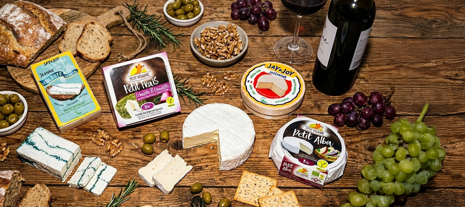 Verschiedene Käsesorten, Wein, Trauben, Oliven, Nüsse und Brot auf rustikalem Holztisch arrangiert.